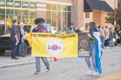Nasir Banks (left) and SALSA Vice President Liana González (right) carry the SALSA banner at the 2022 Bold & Gold Homecoming parade. They are wearing the flags of Latin American countries that are meaningful to them.